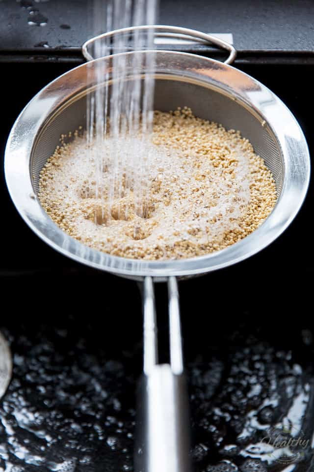 Quinoa in a stainless steel sieve getting rinsed in a black sink