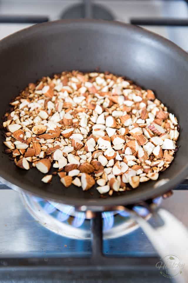 Chopped almonds being toasted in a small non-stick pan on gas range