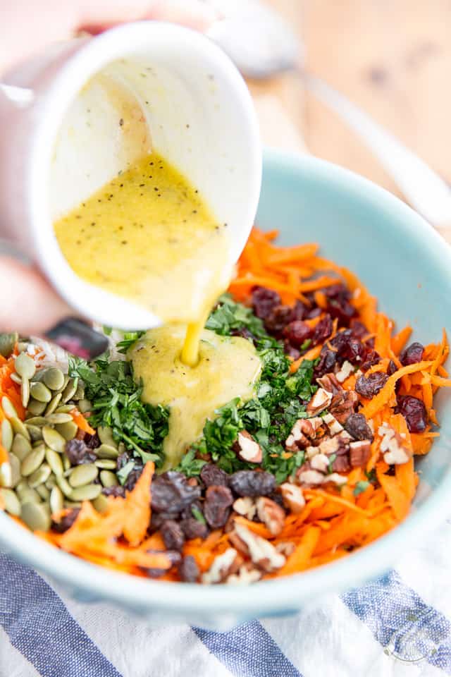A creamy yellow vinaigrette is getting poured over grated carrot salad 
