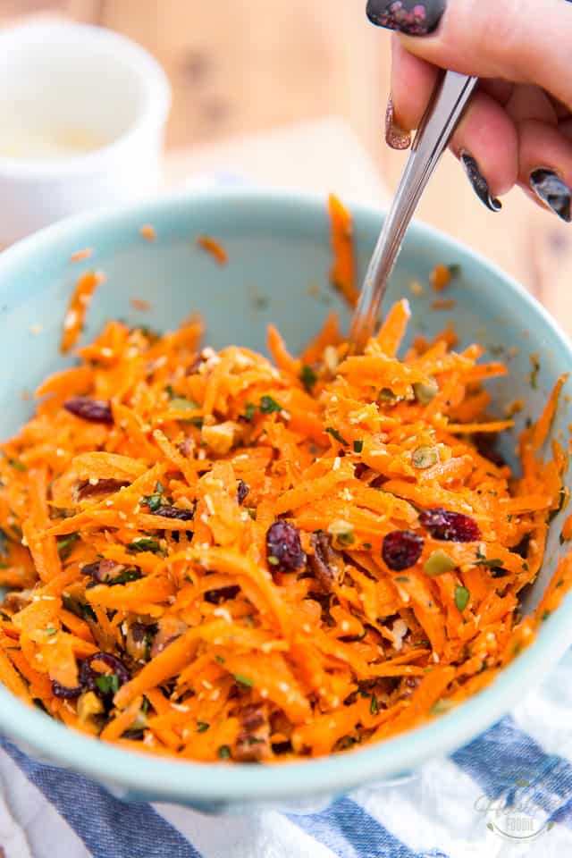 Carrot Salad in a blue bowl, getting tossed with a large spoon