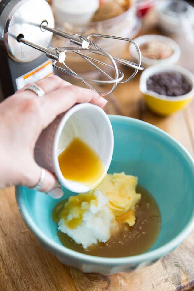 Melted cacao butter is being poured into a blue bowl which already contains coconut oil, ghee and honey