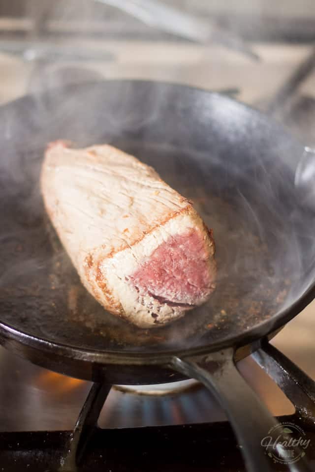 A piece of beef getting seared in a smokey cast iron skillet