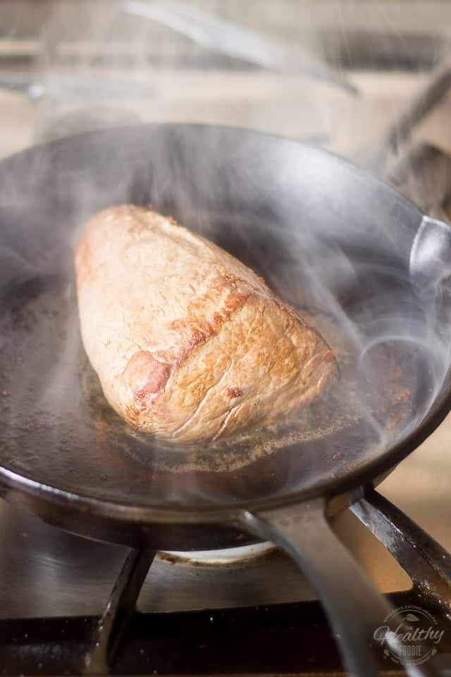 A piece of beef getting seared in a smokey cast iron skillet