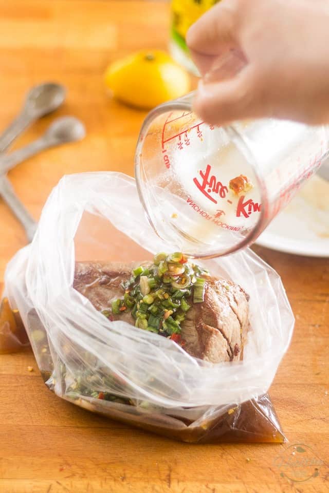 Some herbed marinade being poured into a plastic ziploc bag, over a piece of seared beef