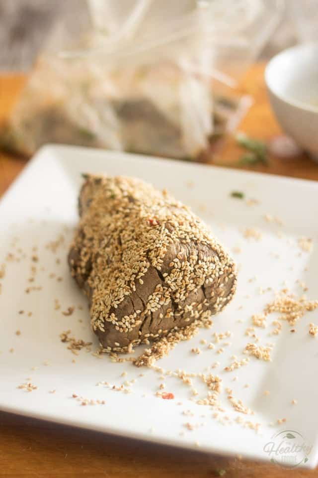 A piece of seared beef covered in toasted sesame seeds, placed on a square white plate