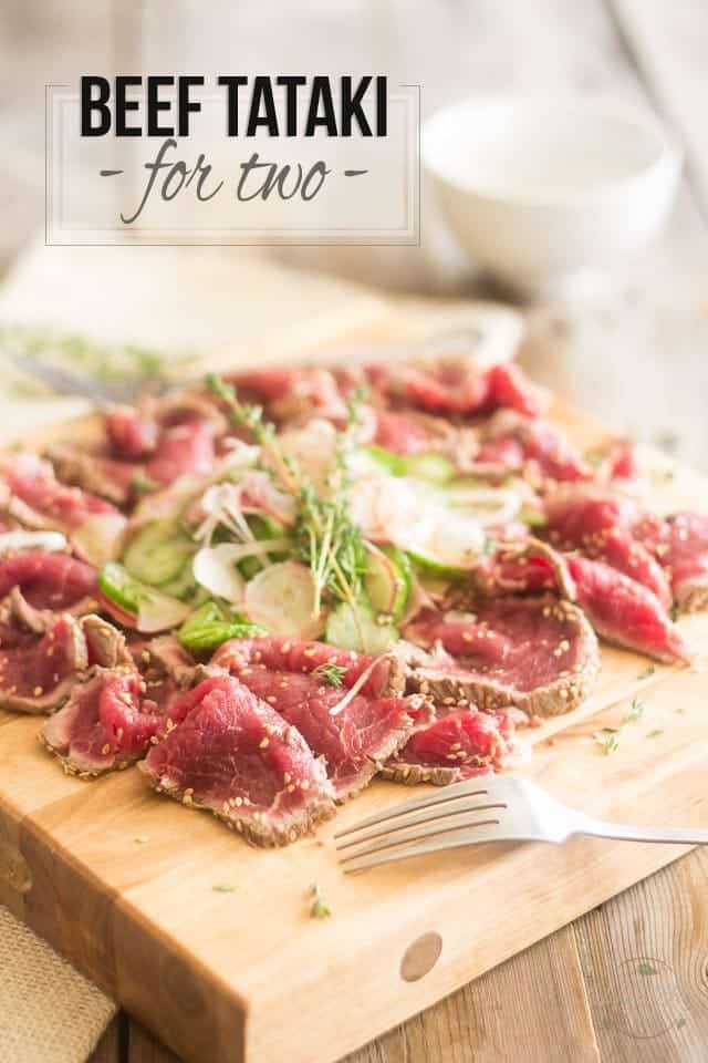 A serving of beef tataki with cucumber and radish salad served on a wooden board with a fork in the foreground