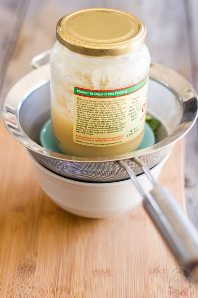 Lebanese cucumbers in a fine meshed sieve with jar of honey sitting on top of them to drain water out