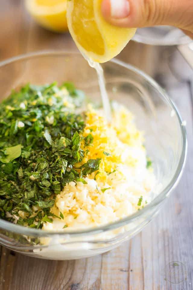 Lemon juice getting squeezed in bowl containing yogurt and chopped herbs