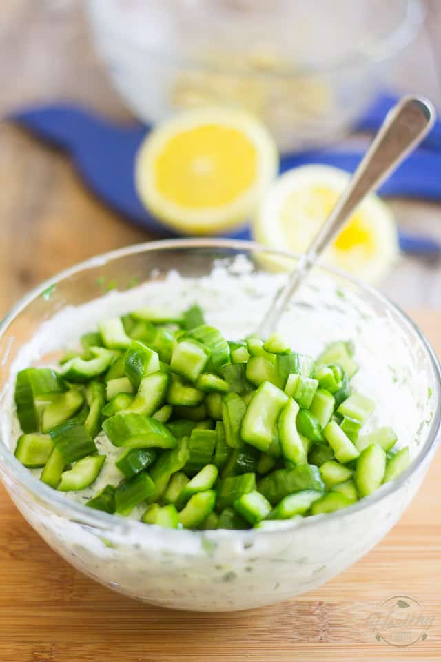 Sliced seeded Lebanese cucumbers in a glass bowl containing yogurt and herbs