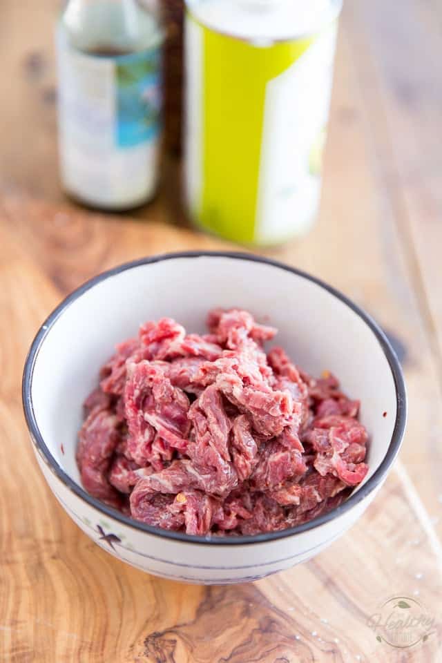 Thin slices of beef in a white bowl with blue border, placed on wooden cutting board