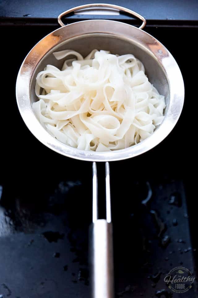 Cooked rice noodles draining in a stainless steel fine meshed sieve over a black sink