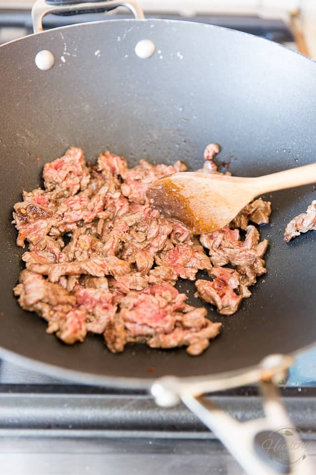 Flank steak being cooked and stirred with a wooden spoon in a non-stick wok