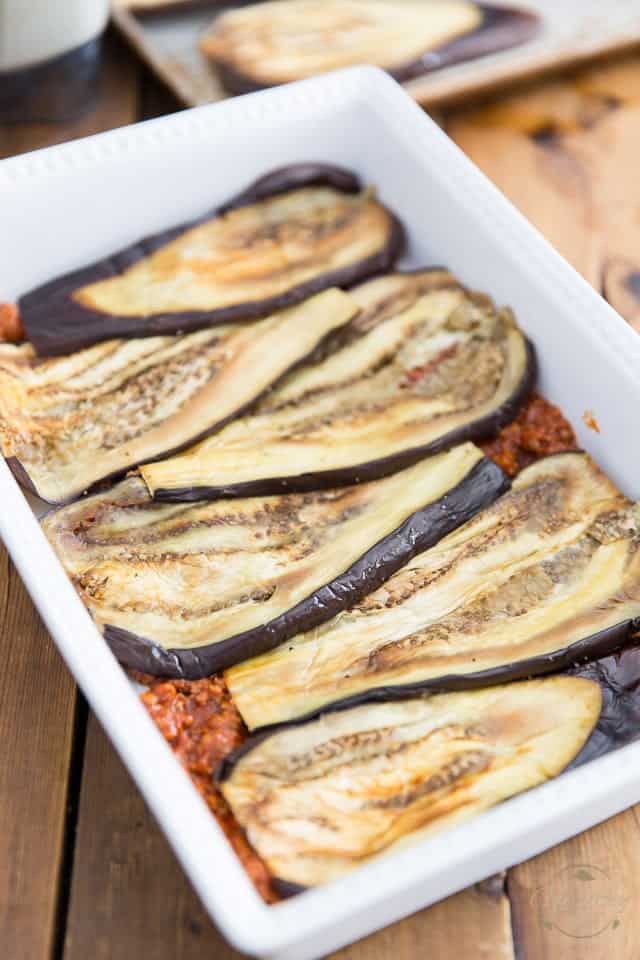 Baked eggplant slices arranged in baking dish over thin layer of meat filling