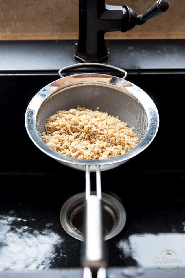 Bulgur draining in a stainless steel fine meshed sieve over a black sink