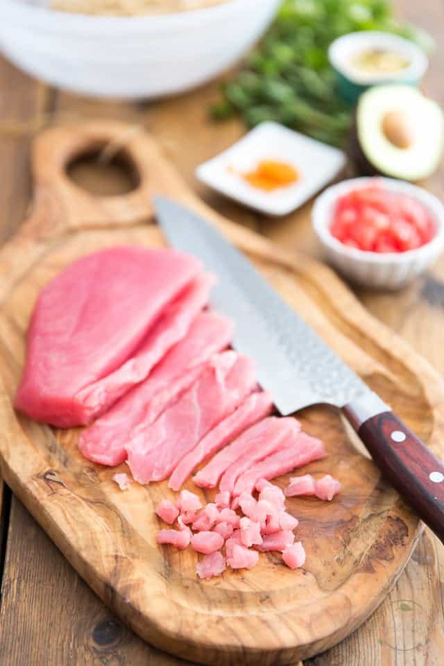 Yellow Fin Tuna Steak on a wooden cutting board, partly sliced and cut into fine pieces, with knife next to it