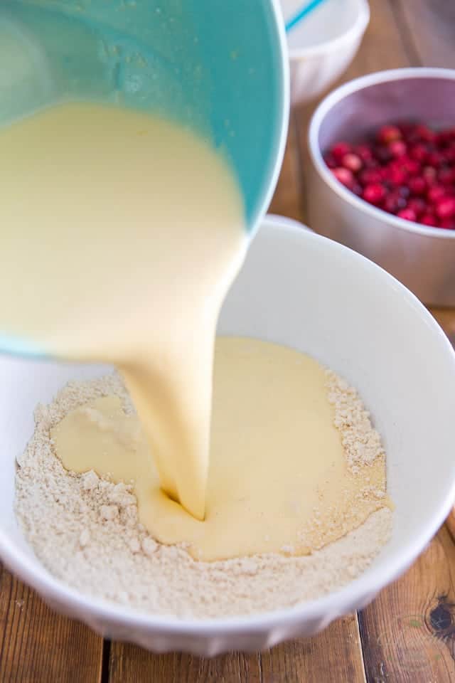 A mixture of sour cream, eggs, buttermilk and honey is being poured into a bowl containing a combination of flours