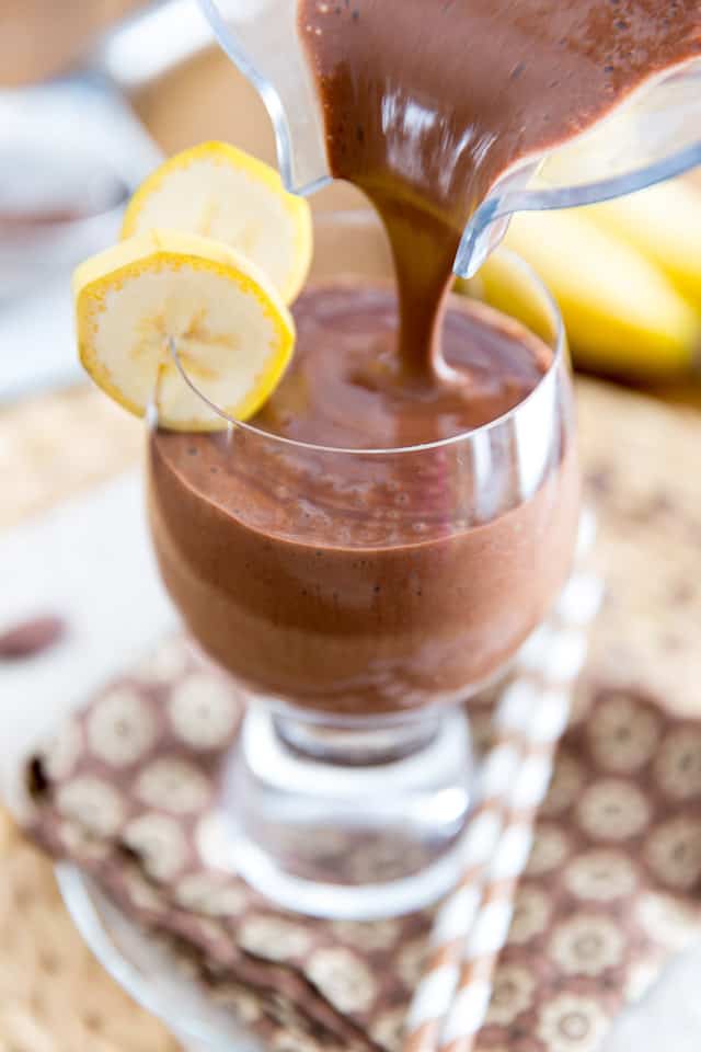 Chocolate Banana Protein Shake is being poured into a glass, garnished with 2 slices of bananas 