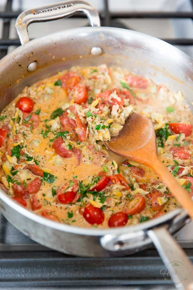 Clam and tomato sauce with fresh cherry tomatoes and parsley in a stainless steel saute pan getting stirred with a wooden spoon
