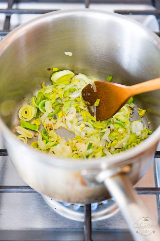 Leeks and garlic cooking in a stainless steel stock pot, stirred with a wooden spoon