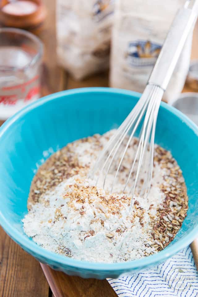 Flours and grains in a blue mixing bowl being mixed with a whisk