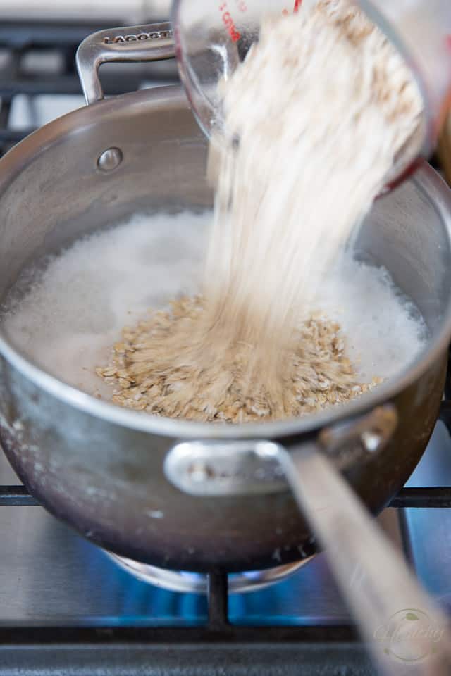 Rolled oats are being added to a saucepan containing boiling milk and coconut water