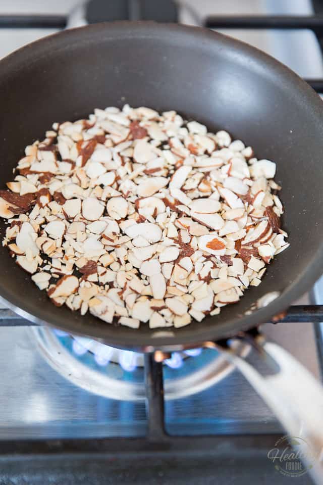 Sliced almonds being toasted in a small non-stick pan on gas range