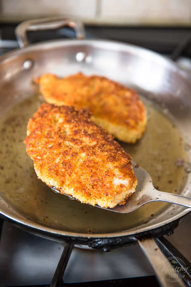 A cooked breaded chicken skillet is getting removed from a stainless steel frying pan with a spatula 