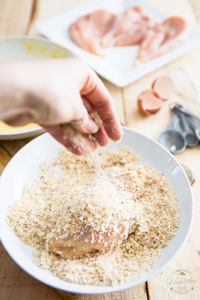 A chicken cutlet in a shallow white bowl getting coated in seasoned breadcrumbs