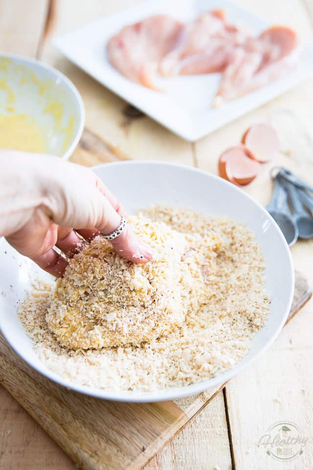 A chicken cutlet in a shallow white bowl getting coated in seasoned breadcrumbs