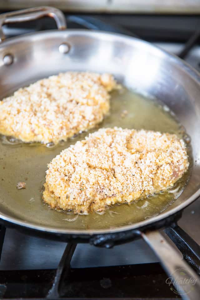 2 breaded chicken cutlets frying in a stainless steel skillet