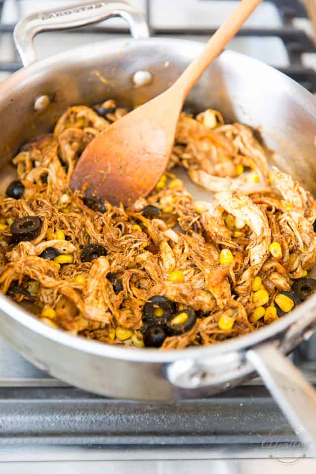 Sliced black olives, corn, chicken and sauteed onions in a stainless steel saute pan