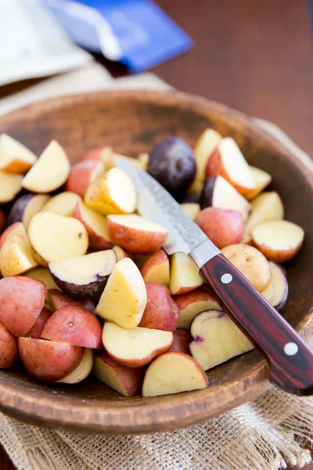 Creamer potatoes cut into quarters in a wooden bowl with knife resting in the pile