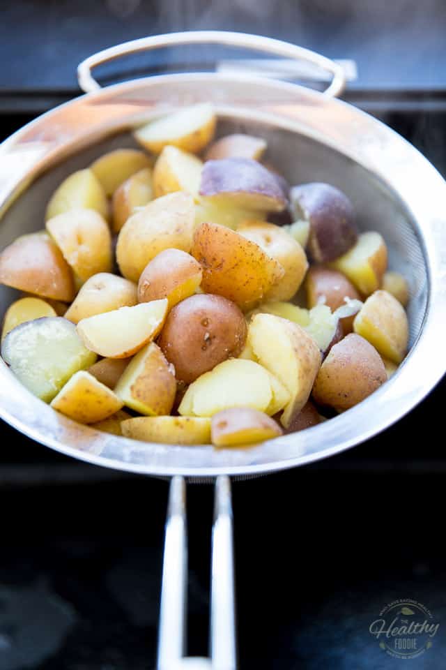Cooked creamer potatoes cooling down in a stainless steel fined meshed sieve over black sink