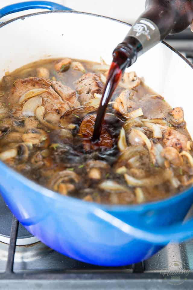 Dark beer is poured into a blue Dutch oven containing mushrooms, onions and seared meat