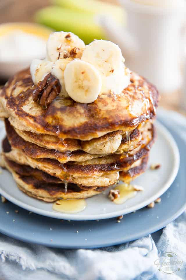 A stack of banana buttermilk pancakes topped with plain yogurt, banana slices, pecans and a little bit of honey