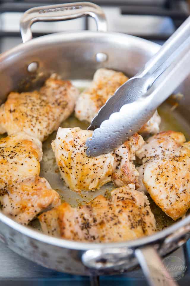 Pieces of chicken browning in a stainless steel saute pan