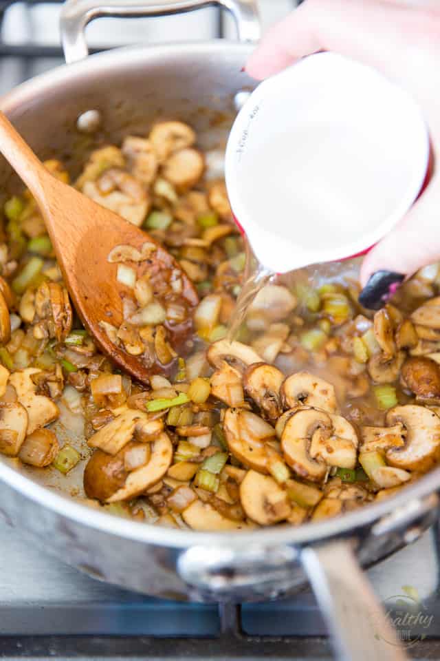 White wine is getting poured into a pan containing sauteed mushrooms, onions and garlic