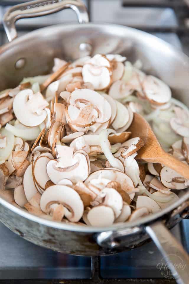 Thinly sliced mushrooms and onions in a stainless steel saute pan