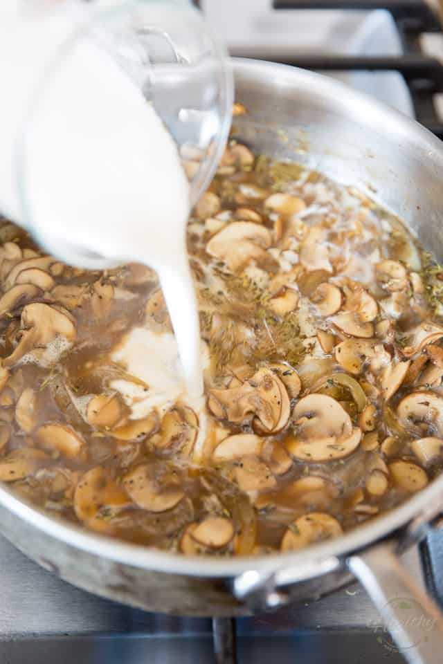 A mixture of sour cream and white wine is being poured into a saute pan containing cooked mushrooms and brown broth