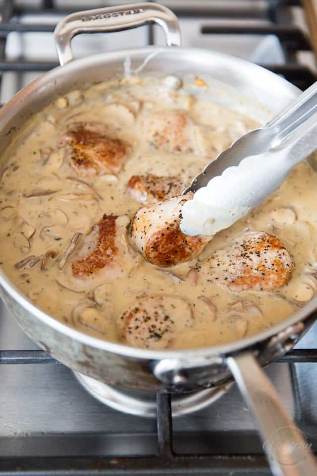Cooked pork medallions are added to a stainless steel saute pan containing a creamy mushroom sauce