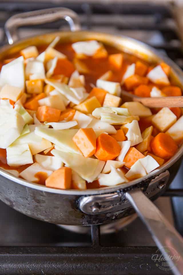 Chunks of raw carrots, cabbage, rutabaga and sweet potatoes getting mixed in a rich tomato sauce simmering in a stainless steel saute pan