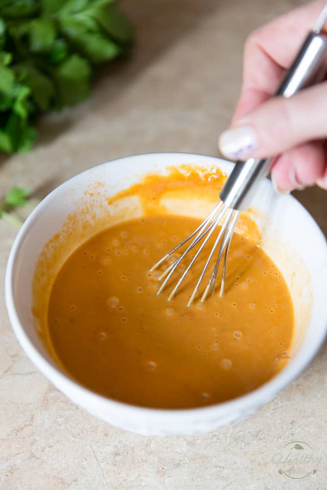 Peanut butter and tomato sauce getting whisked together in a white bowl