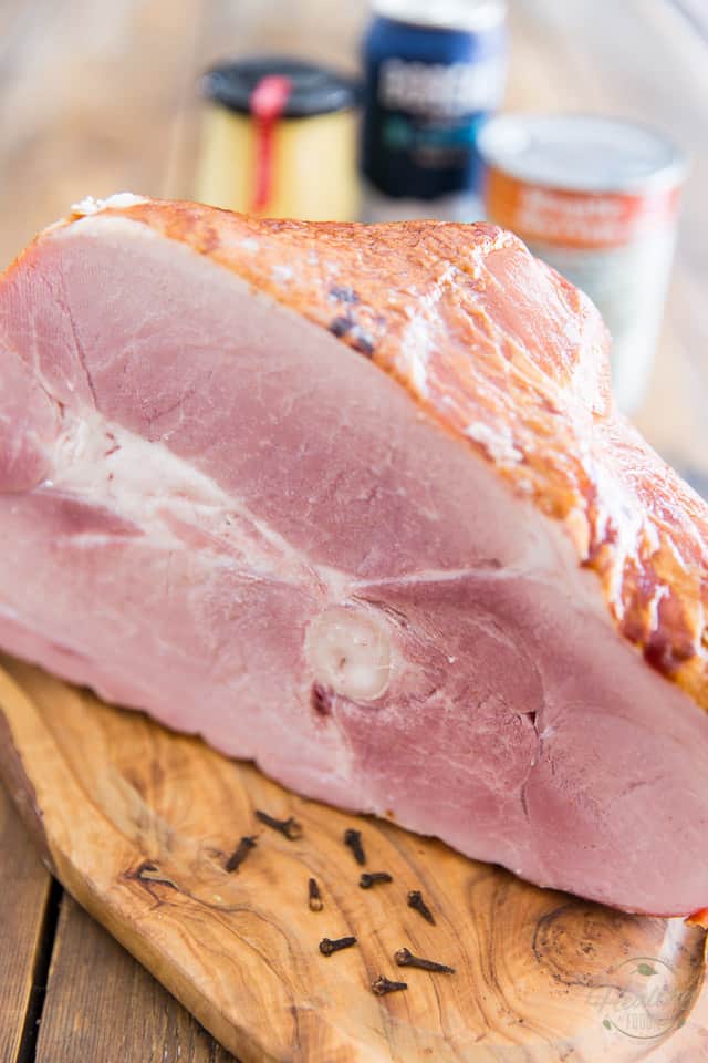 A smoked ham on a wooden cutting board, with a few whole cloves in the foreground