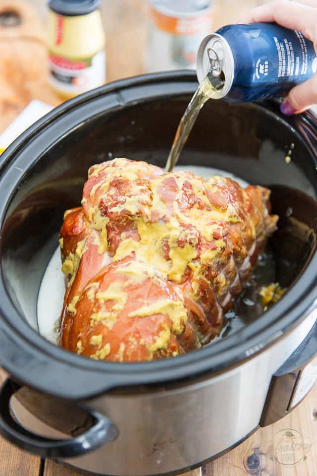A smoked ham basted with Dijon mustard, placed in a slow cooker in which beer is being poured