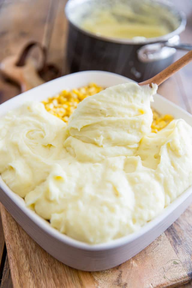 Mashed potatoes being dropped by large spoonfuls over cottage pie