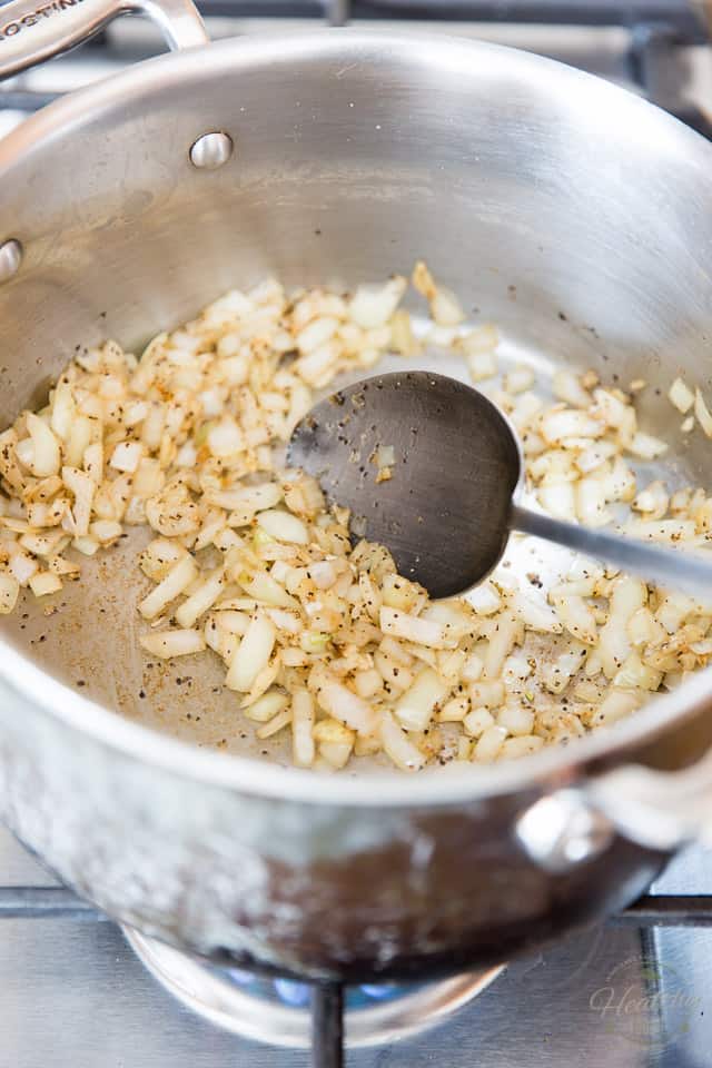 Chopped onions and garlic getting cooked in a large stock pot and stirred with a large stainless steel spoon