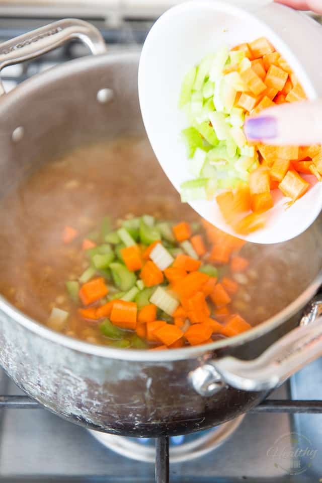 Diced carrots and celery are getting added to a large stock pot of cooking soup