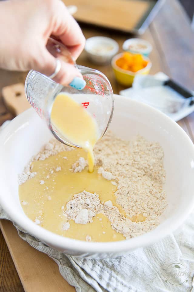 Egg and milk mixture is being poured out of glass measuring cup and into white bowl containing flour and oats