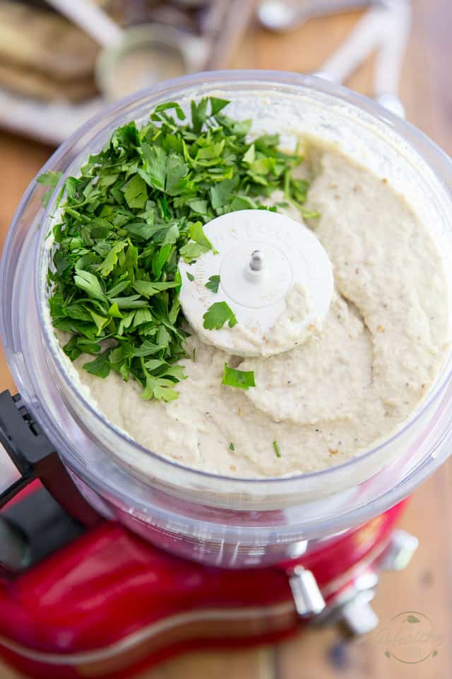 Chopped parsley is being added to the bowl of a food processor containing baba ghanouj