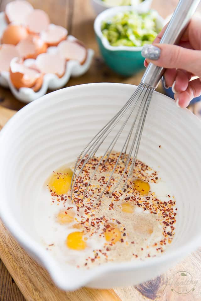 Eggs and spices in a white ceramic mixing bowl getting whisked with large stainless steel whisk